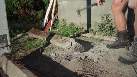 a man is utilizing a hammer to eliminate excess wood from the concrete for the construction of a greenhouse - close up