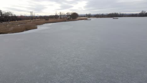 Flight-over-frozen-lake-breaking-ice-in-rural-village,-Poland