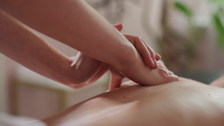 Hands of light skin woman performing gentle back massage on client with folded hands, captured in soft natural light with blurred background, emphasizing calm wellness ambiance and soothing technique