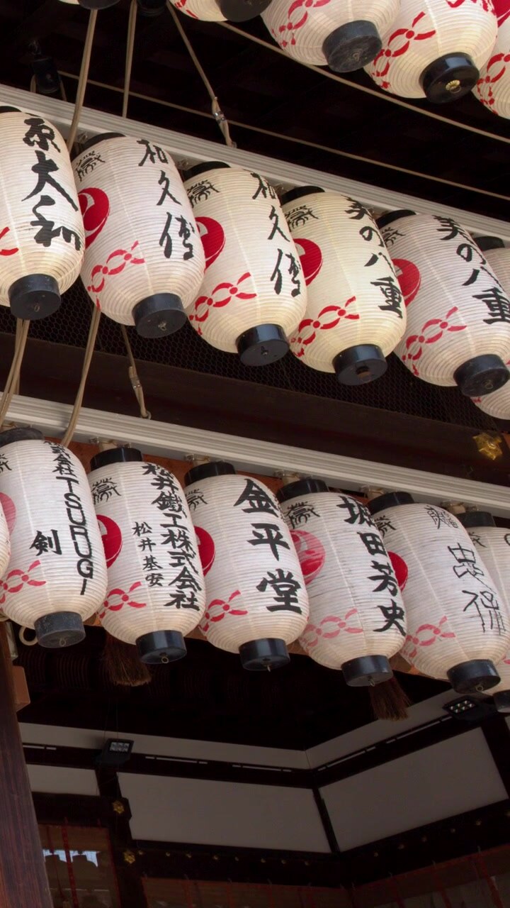 File di lanterne di carta bianche con calligrafia pendono sotto un tetto di tempio in legno a Kyoto