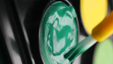 close-up of green paint being mixed with a brush in an art palette