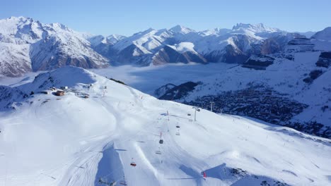 Aerial-view-of-moving-chairlifts-and-several-people-skiing-a-snowy-mountain-on-a-sunny-day