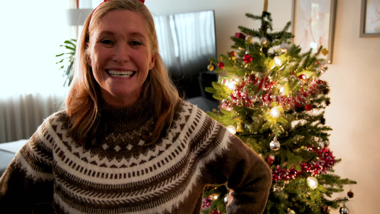 Smiling woman in festive sweater celebrating Christmas at home by tree