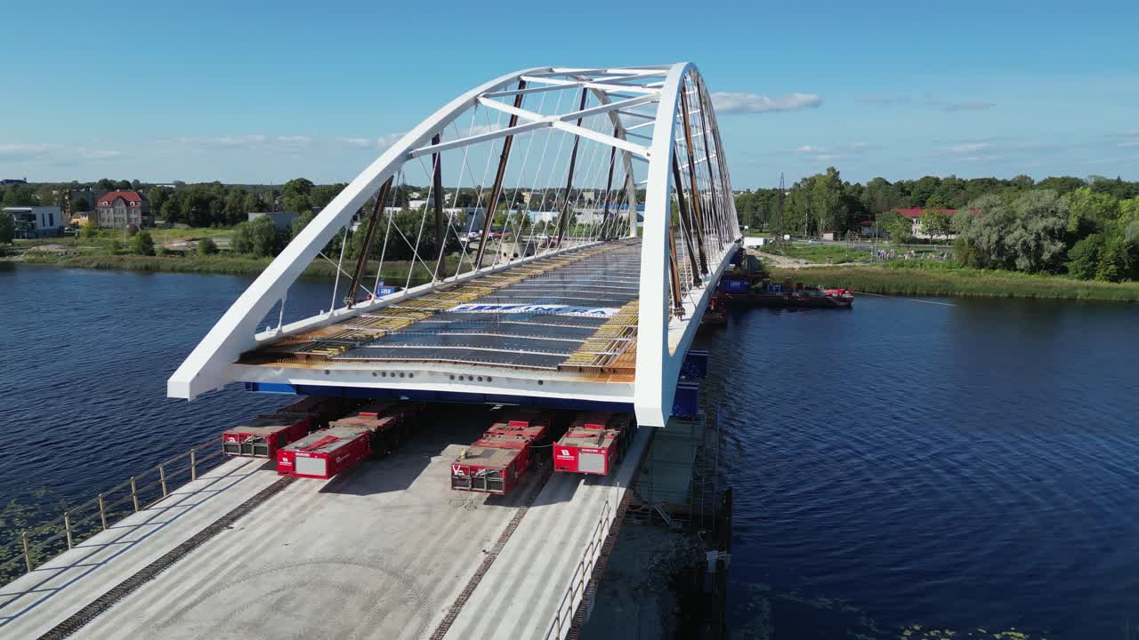 Low aerial orbits new bridge being moved into position over blue river