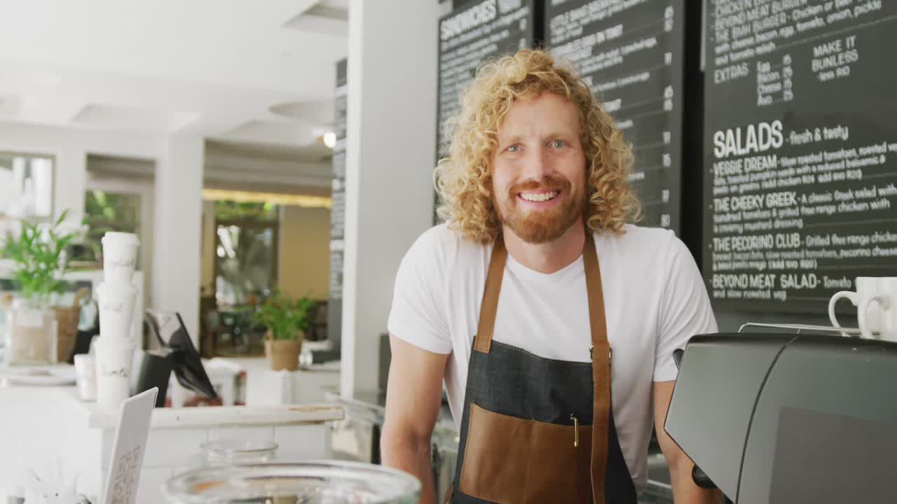 Portrait of happy caucasian male barista smiling behind the counter in cafe