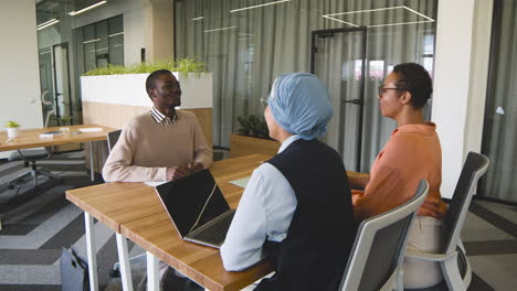 an woman and a muslim woman co workers interview a young man sitting at a table in the office 2