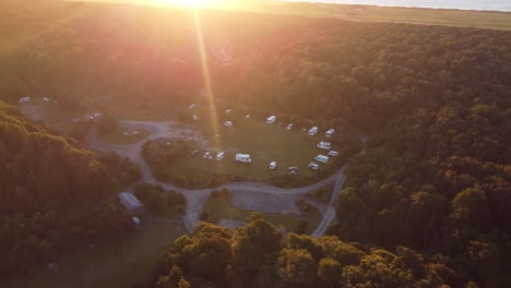 Drone-view-of-a-campground-with-campervans-in-between-forests-during-sunset-at-Lake-Mahinapua,-Hokitika,-West-Coast,-New-Zealand