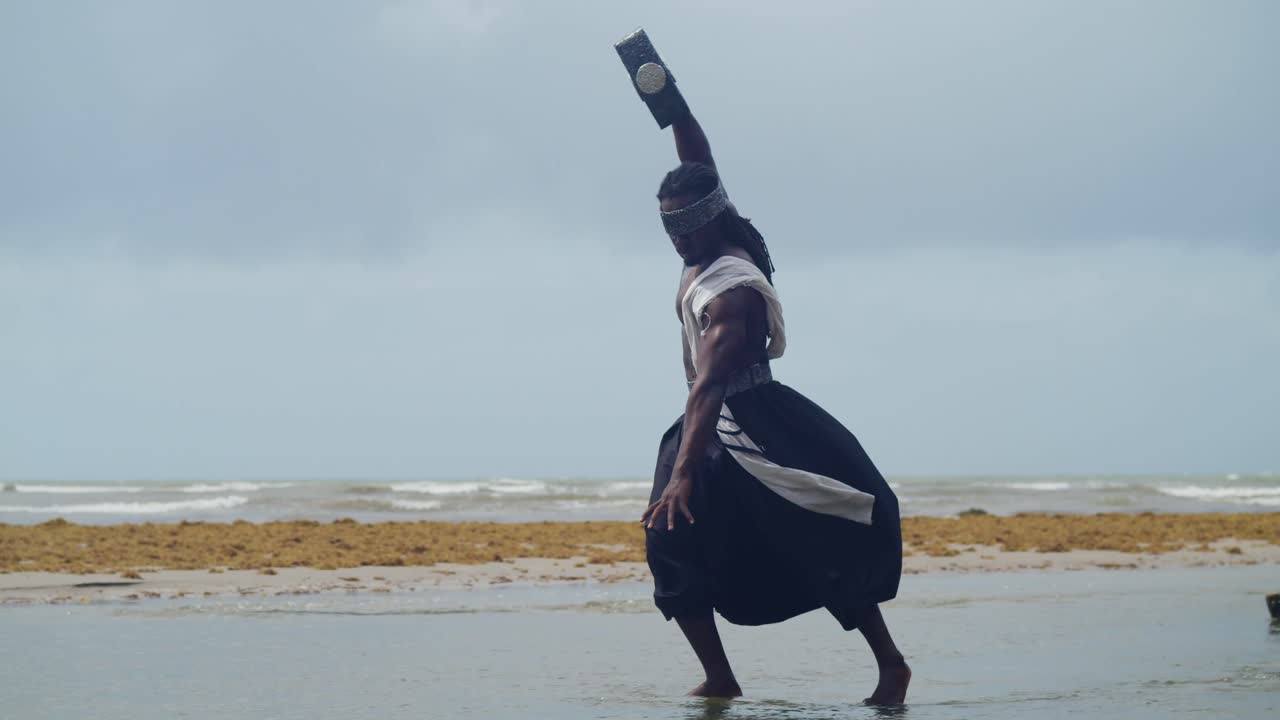 A muscular, dark-skinned man, embodying Nekharis in cosplay, is featured on a tropical beach