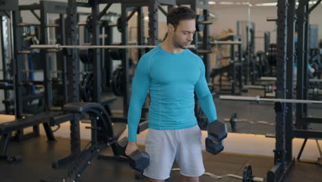 muscular european man lifting weights, doing alternating bicep curls at gym