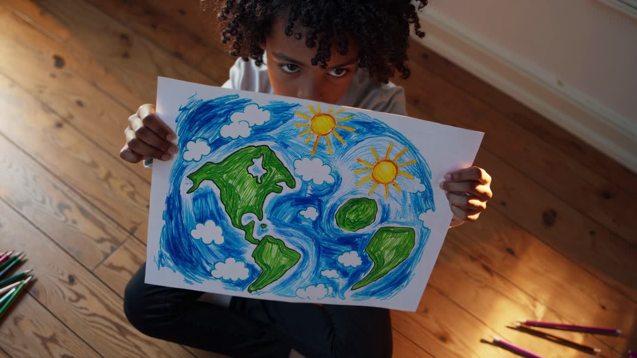 Lapsi istuu puulattialla ja pitää kädessään värikästä Maa-planeetan piirrosta