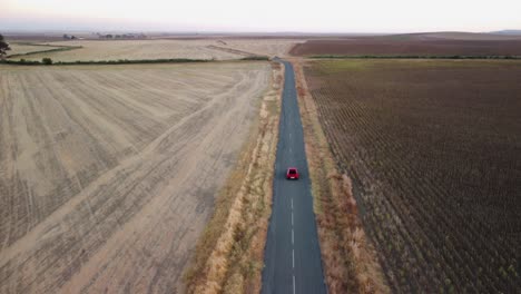 aerial tracking red car on country road tilts up to flat horizon