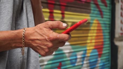 Male-hands-with-chain-bracelet-and-cigarette-using-cell-phone-in-street