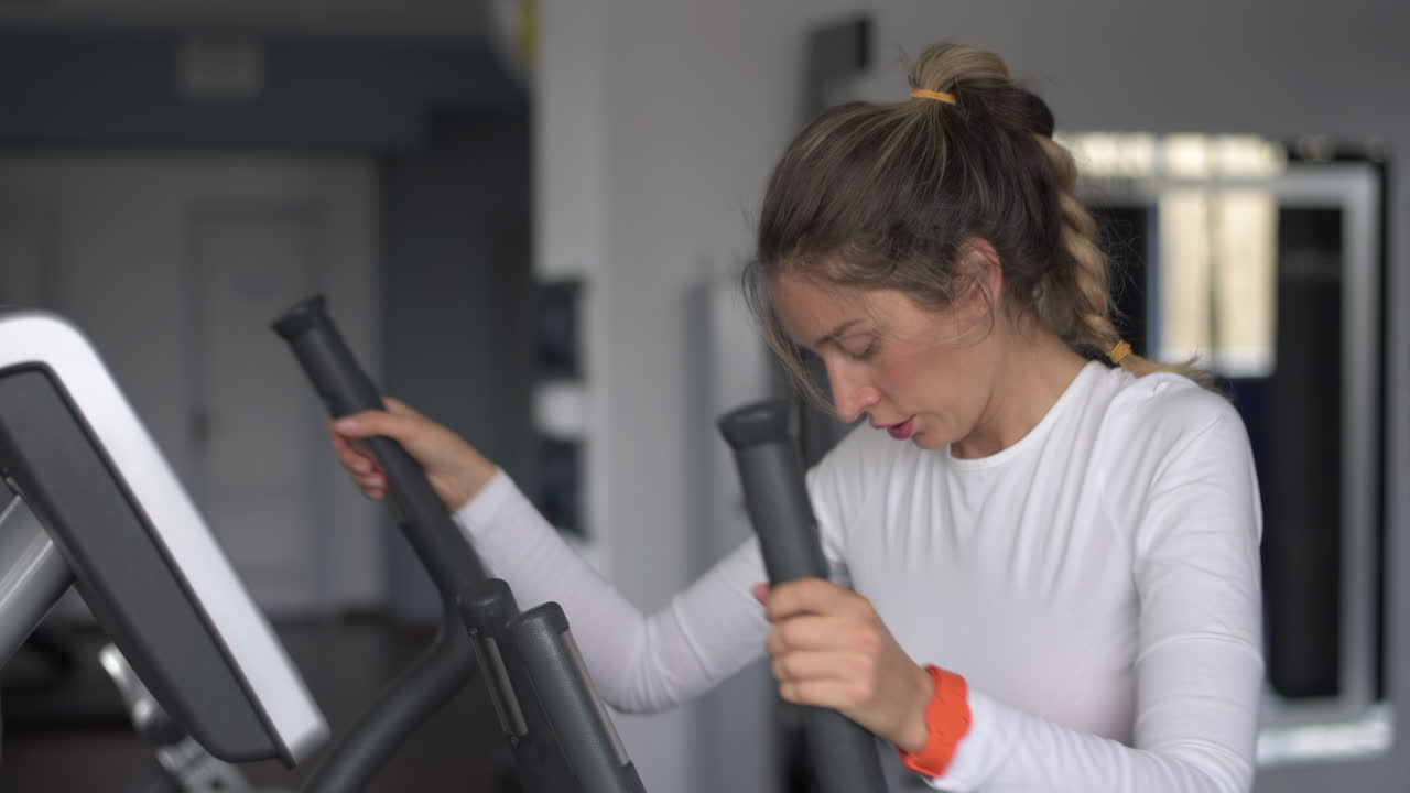 Woman in white activewear working out on the elliptical machine at the gym