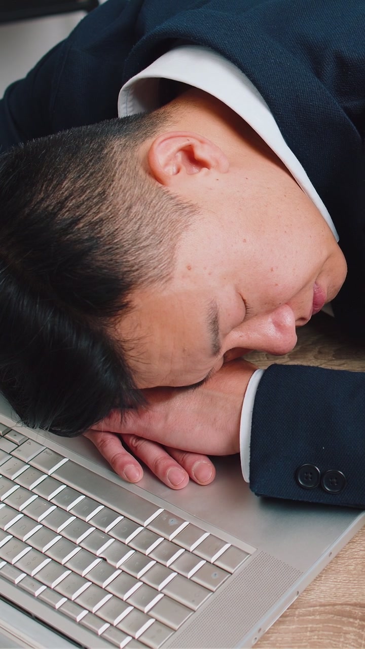 Un uomo d'affari annoiato e addormentato, un operaio che lavora al portatile, appoggiato alle mani, che si addormenta al tavolo dell'ufficio.