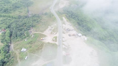 aerial view of rural single-track road on green hills, seen from above fog and clouds on wet season