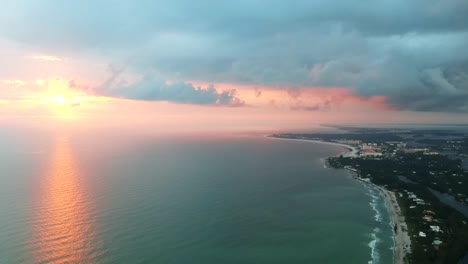 High-aerial-landscape-shot-of-a-peaceful-orange-pink-sunset-above-the-Florida-coast,-the-sun-reflects-in-the-ocean-water-during-this-golden-hour