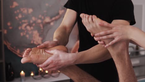 Close-up-of-hands-of-female-and-male-massage-therapists-performing-four-hand-massage-on-the-feet-of-a-sporty-man