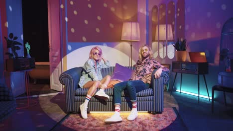 young caucasian woman and man in stylish clothes sitting on sofa and talking in a retro party at home