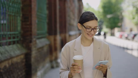 Woman Walking Down City Street with Coffee and Phone