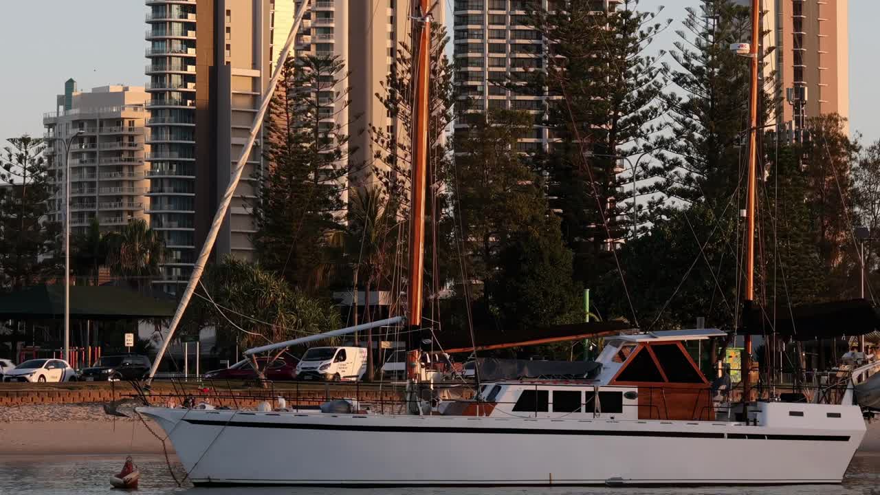 A serene view of a sailboat anchored near a city waterfront during sunset.