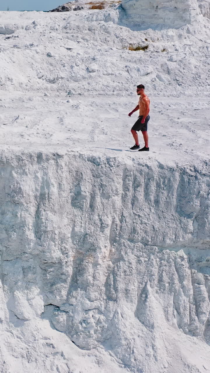 Young sporty man in white mountains. Healthy man without shirt walking along rocky canyon in a warm sunny day. Aerial view. Vertical video
