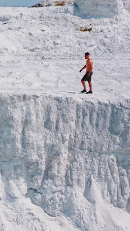 young sporty man in white mountains. healthy man without shirt walking along rocky canyon in a warm sunny day. aerial view. vertical video