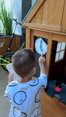 little boy stands at the small wooden play house. happy kid touches the clock on the wall. high angle view. vertical video.