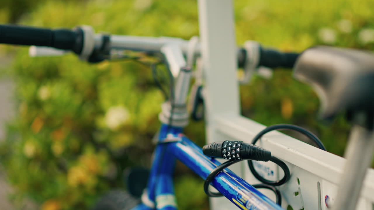 Close up of a cable lock securing a blue bike to a white fence