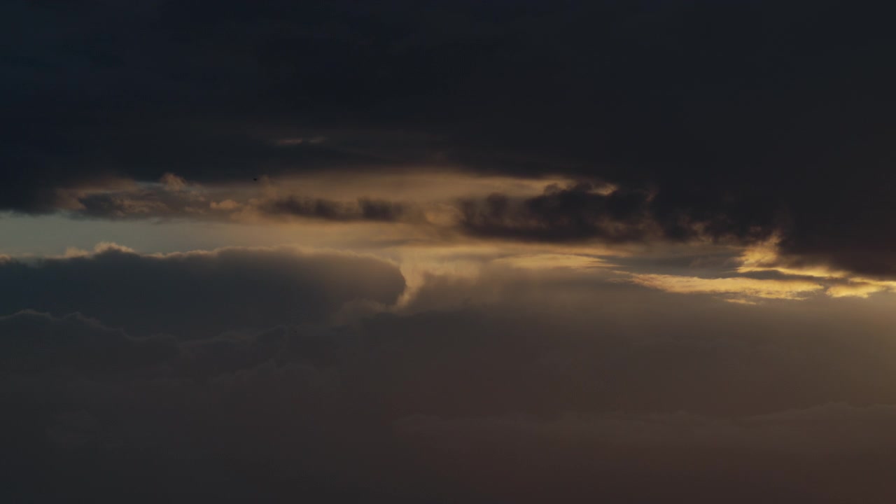 Smalle stråler af solnedgangslys siver ind mellem tætte stormlag og afslører skiftende tekstur på den mørknende himmel