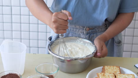 Mujer-Asiática-Joven-Revolviendo-La-Crema-Para-Hacer-Pastel-De-Tiramisú-Con-Una-Espátula