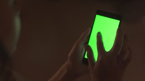 persona que utiliza un teléfono inteligente con una pantalla verde por la noche