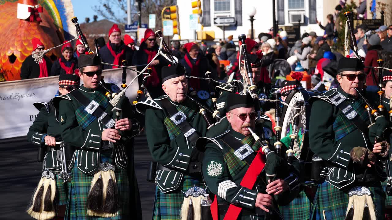 Marching Band playing European bagpipes and drums while marching down the street with a large Turkey Float and Plymouth 400 sign in the background - 2019 Thanksgiving Parade Plymouth, Massachusetts