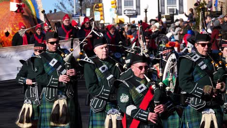 marching band playing european bagpipes and drums while marching down the street with a large turkey float and plymouth 400 sign in the background - 2019 thanksgiving parade plymouth, massachusetts
