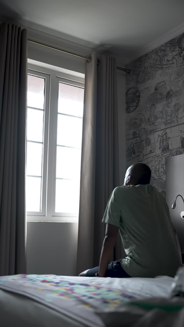 Man Looking Through Window While Sitting in Well-Decorated Hotel Room. vertical video