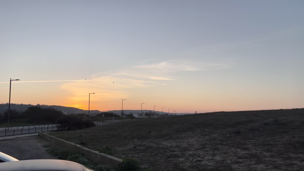 Peaceful sunset view over quiet road with streetlamps, surrounded by hills, scenic nature view