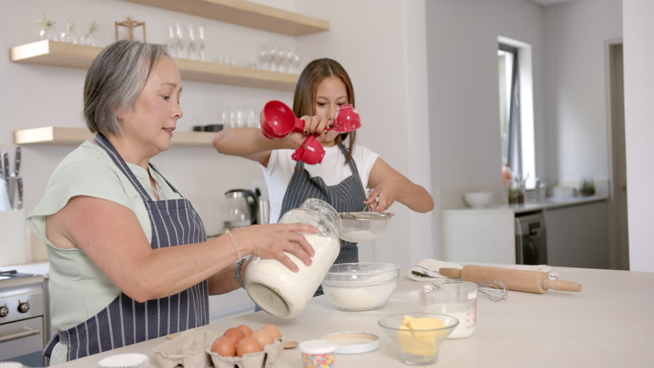 Baking together, asian grandmother and child measuring flour and sifting in kitchen