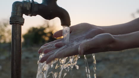 Frau-Wäscht-Sich-Bei-Sonnenuntergang-Auf-Einem-Ländlichen-Bauernhof-Die-Hände-Unter-Fließendem-Wasser,-Das-Aus-Dem-Wasserhahn-Fließt