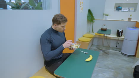 Cheerful-Positive-Sportsman-Enjoys-Eating-Salad-for-Lunch-After-Training-at-Small-Gym-Cafe