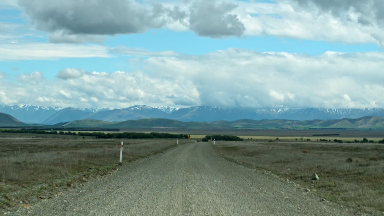 vista a bordo de un viaje lento a lo largo de un camino de tierra hacia majestuosas montañas cubiertas de nieve bajo el sol