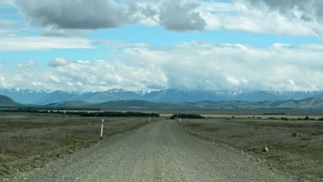 onboard view of a slow drive along a dirt road towards majestic snow-capped mountains in sunshine