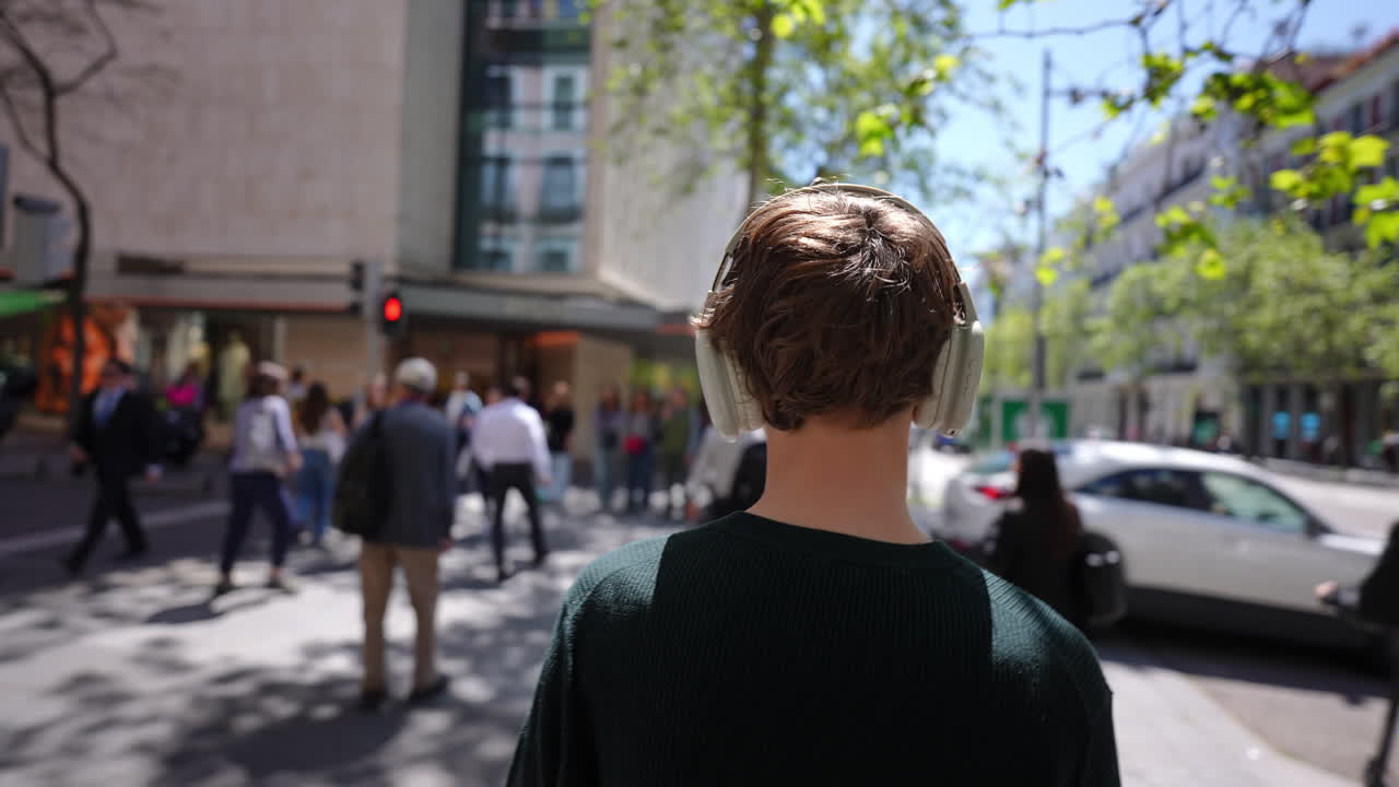 Young tourist walking along city street, immersing in music while navigating urban environment with wireless headphones and carefree attitude