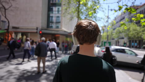 young tourist walking along city street, immersing in music while navigating urban environment with wireless headphones and carefree attitude