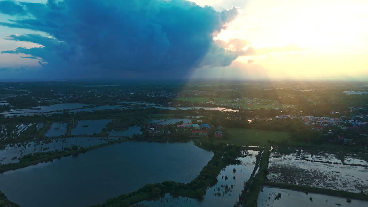 Cinematic 4K aerial of dramatic storm clouds and golden sun rays illuminating wetlands and farmlands—perfect for documentaries, nature, and inspirational projects