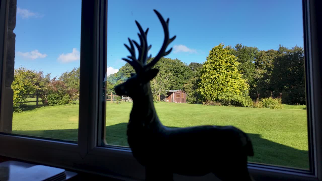 Stag silhouette ornament on a window sill overlooking a bright garden and trees