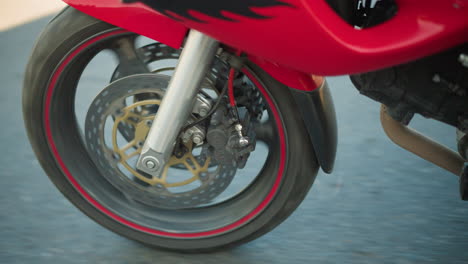 a close-up of a motorcycle's front wheel spinning on a smooth, tarred road, the tire and brake components are in focus