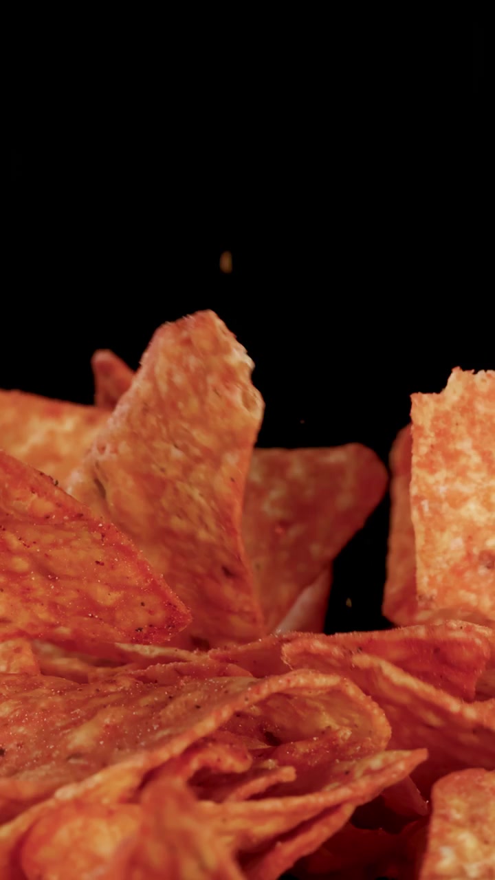 Chips di tortilla croccanti cadono al rallentatore su una pila, illuminazione drammatica, sfondo nero
