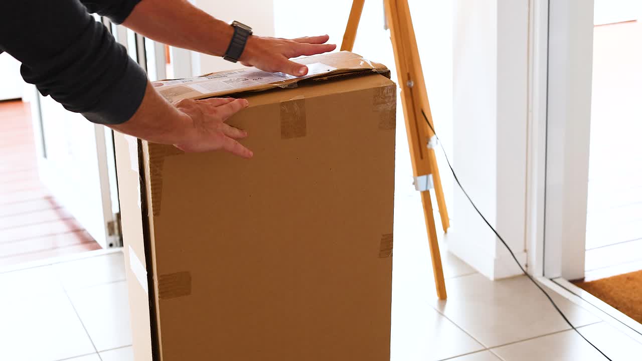 Hands carefully open a large cardboard box in a bright, sunlit room. Natural lighting and minimalistic decor create a calm atmosphere