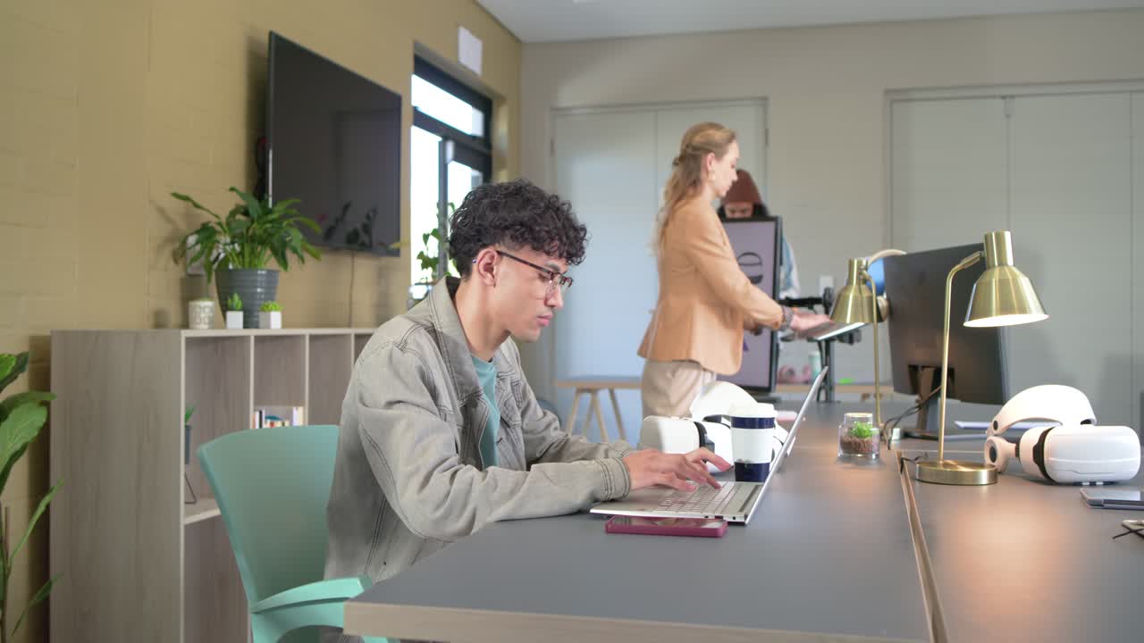 Hombre de mediana edad con chaqueta vaquera escribiendo y haciendo una pausa con el portátil en un escritorio de coworking, espacio para copiar