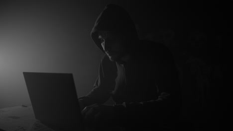 pirata informático con capucha y portátil en una habitación oscura