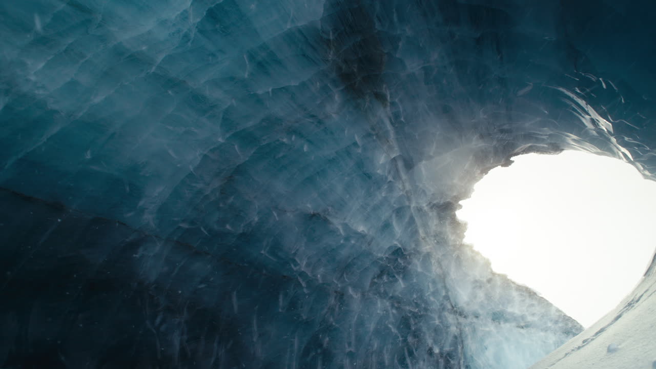 revelando un gran túnel azul de una cueva de hielo ártico con nieve cayendo lentamente